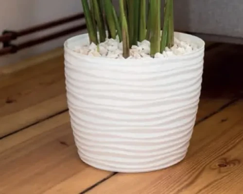 Biała doniczka Sahara Round z ozdobnym kwiatem postawiona na drewnianym stole