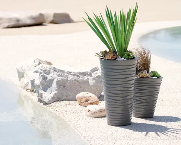 Donica Sand 40 cm kolor mocca w aranżacji z roślinami. Ozdobne doniczki z posadzonymi zielonymi roślinami stoi na piasku.