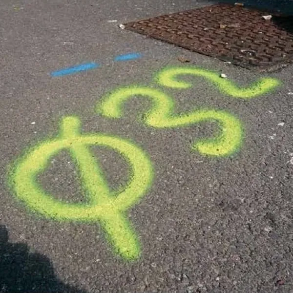 Jaskrawe oznaczenia geodezyjne z symbolem, namalowane fluorescencyjną farbą na ciemnym asfalcie.
