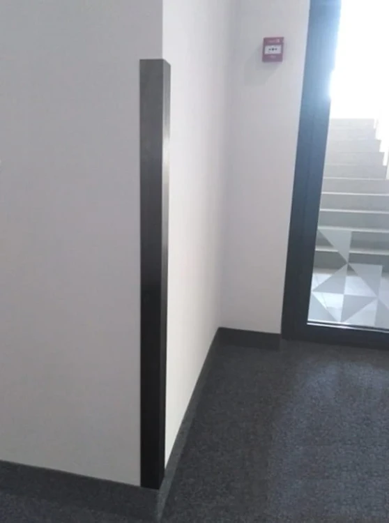 Kątownik ze stali nierdzewnej 50x50 mm zamontowany na narożniku ściany w nowoczesnym korytarzu biurowym.