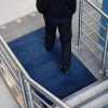 Chodnik antypoślizgowy Strongmata w odcieniu granatowym leżący na kafelkach na klatce schodowej.