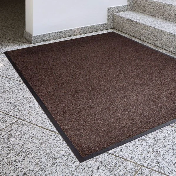 Chłonna wycieraczka tekstylna Strongmata 85 x 120 cm w kolorze ciemnego brązu leżąca płasko w korytarzu biurowym przed schodami.