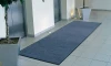Długa wycieraczka osuszająca Strongmata 150x400 cm przylegająca płasko do podłogi przed strefą wind w biurowcu.