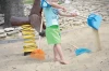 Małe dziecko w piaskownicy trzymające łopatkę Load Baby Alu obok leżących czerwonych i niebieskich grabek dziecięcych Focus Baby.
