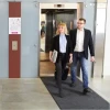 Grafitowa mata tekstylna 85x300 cm Monokolor rozłożona zbiera wilgoć i brud przed windą z przechodzącą kobietą i mężczyzną.