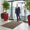 Brązowa mata do butów Monokolor rozłożona przy automatycznych drzwiach w strefie wejściowej nowoczesnego biura z przechodzącym mężczyzną.