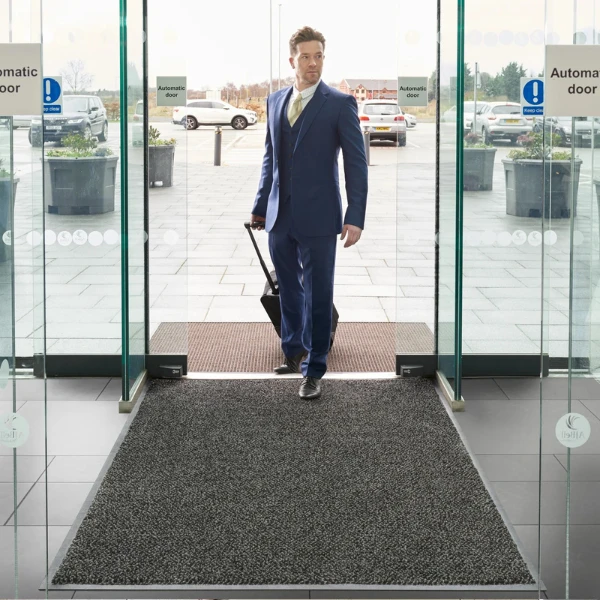 Duża czarna wycieraczka podgumowana Marathon rozłożona w nowoczesnej strefie wejściowej lotniska.