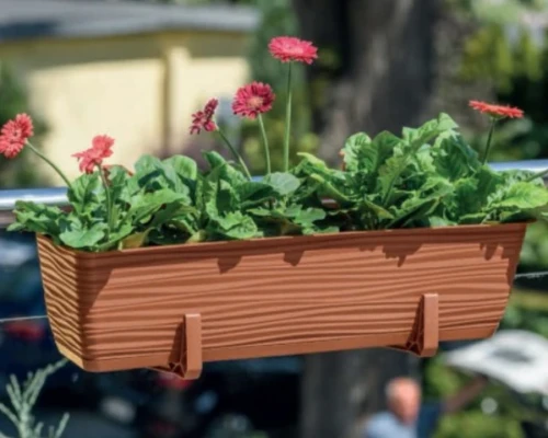 Prostokątna doniczka z gęstą roślinnością wisząca na barierce balkonowej w słoneczne popołudnie.