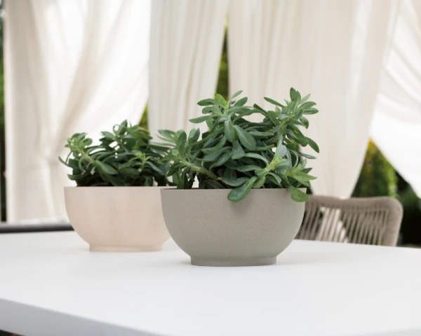 Dekoracyjne donice plastikowe z roślinami ustawione na stole na tarasie jako stylowy element oprawy zewnętrznej